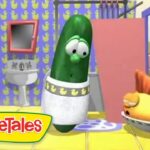 Green pickle character wearing a diaper stands in a colorful VeggieTales bathroom set, with another character resting nearby.