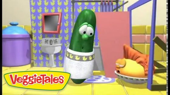 Green pickle character wearing a diaper stands in a colorful VeggieTales bathroom set, with another character resting nearby.