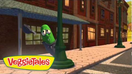 Animated green cucumber character peeks from behind a lamppost on a sunny brick sidewalk, VeggieTales logo in the corner.