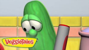 Larry the Cucumber from VeggieTales looks at a large marker in a colorful tiled set, logo visible in the corner.
