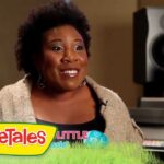 Smiling woman being interviewed in a recording studio, with VeggieTales branding visible on the monitor and a colorful footer graphic.