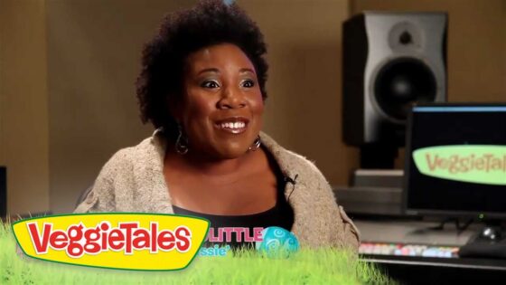Smiling woman being interviewed in a recording studio, with VeggieTales branding visible on the monitor and a colorful footer graphic.