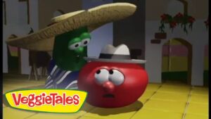 Tomato character wearing a hat looks surprised as a green veggie behind him leans over in a kitchen-like room; VeggieTales logo in corner.
