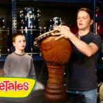 Man shows a large wooden drum to two kids in a music store; VeggieTales logo appears in the corner.