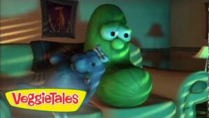 Green cucumber character from VeggieTales standing in a living room with a blue vegetable beside him; VeggieTales logo appears in the bottom-left corner.