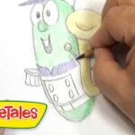 Close-up of a hand coloring a green VeggieTales character on a coloring sheet with a pencil; VeggieTales logo in the lower-left corner.
