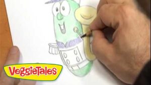 Close-up of a hand coloring a green VeggieTales character on a coloring sheet with a pencil; VeggieTales logo in the lower-left corner.