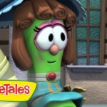 Cartoon green vegetable with brown curled hair and pink glasses stands outside a building; VeggieTales logo in the corner.