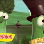 Two green VeggieTales characters stand outdoors, one with a monocle and broccoli top, the other wearing a tall hat and checkered scarf, smiling at the camera.