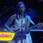 Female singer performing on stage, playing an acoustic guitar and singing into a mic, VeggieTales logo visible in the corner.