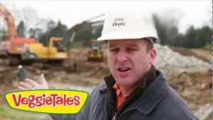 Construction site speaker wearing a hard hat, with machinery in the background; VeggieTales logo in the lower-left corner.