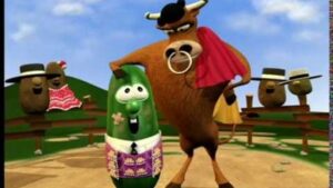 Cartoon bull wearing a red cape stands beside a cheerful green vegetable character in a field scene with spectators.