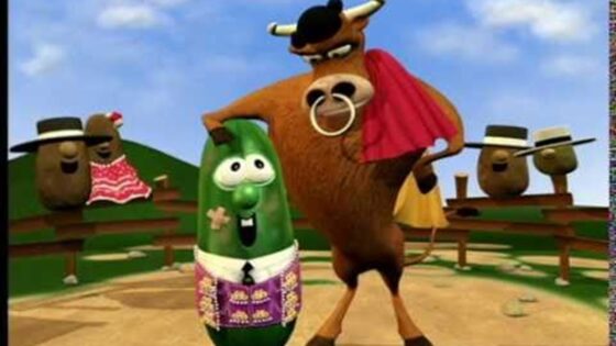 Cartoon bull wearing a red cape stands beside a cheerful green vegetable character in a field scene with spectators.