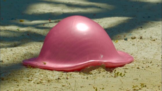 Pink inflatable beach toy shaped like a jellyfish resting on sandy ground at the beach
