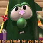 Cartoon green creature dressed as a Christmas tree with presents around, looking toward the viewer.
