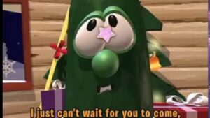 Cartoon green creature dressed as a Christmas tree with presents around, looking toward the viewer.