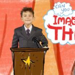 Young boy in a suit speaks at a wooden podium with a microphone, colorful stage backdrop and a large 'Imagine That!' speech bubble behind him.