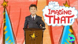 Young boy in a suit speaks at a wooden podium with a microphone, colorful stage backdrop and a large 'Imagine That!' speech bubble behind him.