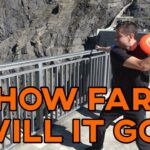 Man at a cliff overlook throws a frisbee while holding a selfie stick; large orange text reads 'HOW FAR WILL IT GO?'