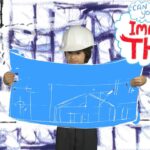 Child in a white hard hat holds a large blue blueprint showing a building sketch, set against a white-and-purple doodle background with a 'Imagine That!' speech bubble