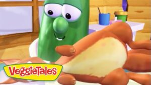 VeggieTales scene: a smiling green cucumber character holding a hot dog bun in a kitchen setting, with the VeggieTales logo visible in the corner.