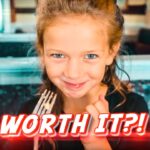 Smiling young girl holding a fork in a restaurant, with bold 'WORTH IT?!' text overlay.