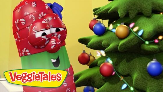 VeggieTales character with candy-cane wrap beside a decorated Christmas tree with colorful ornaments and lights, logo visible on the lower left.