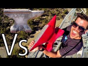 Man wearing sunglasses on a tall metal structure, smiling while holding a red rocket toy; large 'VS' text on left.