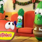 VeggieTales characters in a festively decorated living room with a Christmas tree; a cucumber in a reindeer sweater chats with an orange tomato.