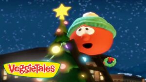 Cartoon VeggieTales character in a green hat decorating a Christmas tree with colorful lights under a snowy night sky; VeggieTales logo bottom left.