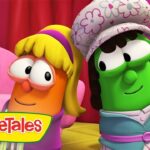 Two VeggieTales characters pose together in a colorful pink set—a carrot with blonde hair and glasses beside a green cucumber wearing a floral hat.