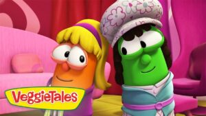 Two VeggieTales characters pose together in a colorful pink set—a carrot with blonde hair and glasses beside a green cucumber wearing a floral hat.