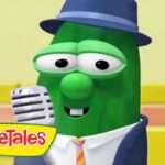 Green VeggieTales bean character wearing a blue hat and suit, smiling while singing into a vintage microphone on a colorful stage. Logo reads VeggieTales.