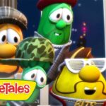 Group of VeggieTales characters peeking from a crate in a city at night, with one yellow veggie wearing white sunglasses and a mustache, a green veggie in a red cap, and others in hats nearby; VeggieTales logo in the corner.