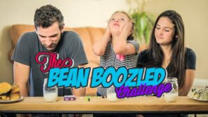Three people sit at a table for a Bean Boozled Challenge; a girl in striped shirt looks stressed, while a man and a woman watch. Milk and jelly beans on the table are visible.