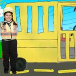 Child wearing a reflective safety vest and hat stands next to a large yellow bus drawing in a bright, colorful scene.