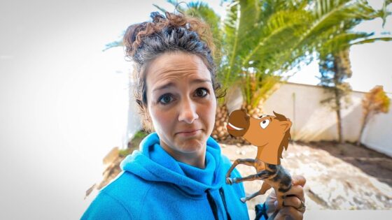 Young woman in a bright blue hoodie outdoors holding a small cartoon horse figure near her face, with palm trees in the background.