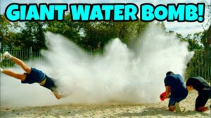 People outdoors get soaked by a huge water explosion; one person is mid‑air from the splash while two others kneel nearby with a water container. Bold text reads 'GIANT WATER BOMB!'