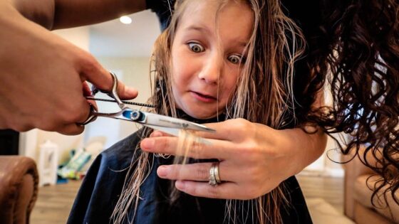 Hairdresser cutting a young girl's hair while the girl looks astonished, eyes wide as scissors hover near her strands