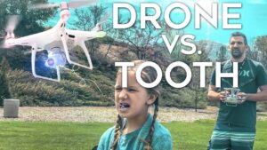 Thumbnail for a video showing a white quadcopter flying near a girl in a park while a man with a controller watches, overlaid with the text 'DRONE VS. TOOTH'