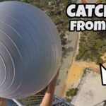 Aerial view of a person reaching for a large gray spherical ball suspended from a tall structure, with the caption “CATCHING FROM 45m!”.