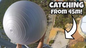 Aerial view of a person reaching for a large gray spherical ball suspended from a tall structure, with the caption “CATCHING FROM 45m!”.