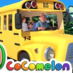 Yellow school bus with a cheerful driver and children looking out the windows on a sunny street, Cocomelon logo in the corner.