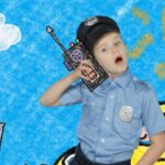 Boy in a police uniform talking into a toy radio against a bright crayon-drawn backdrop (blue sky, sun, buildings).