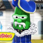 Green cucumber character wearing a blue royal coat with a white fur collar and hat, standing in a castle setting; VeggieTales logo visible on screen edge.
