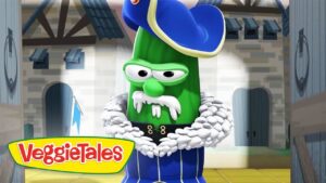 Green cucumber character wearing a blue royal coat with a white fur collar and hat, standing in a castle setting; VeggieTales logo visible on screen edge.