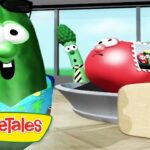 Animated VeggieTales scene with a green cucumber wearing sunglasses and a blue floral shirt, and a red tomato nearby, a broccoli stalk in the background, and a beige suitcase; VeggieTales logo in the corner.