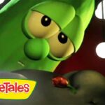 Close-up of a green VeggieTales cucumber character with big eyes, logo in the bottom-left corner.