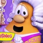 Animated carrot character with a white powdered wig and purple outfit, in a VeggieTales scene with the logo visible at the bottom left.