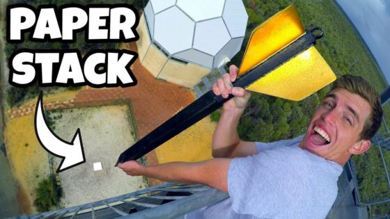Smiling man on a tall platform holds a long pole with a yellow blade, high above ground beside a tower, with 'PAPER STACK' text overlay.